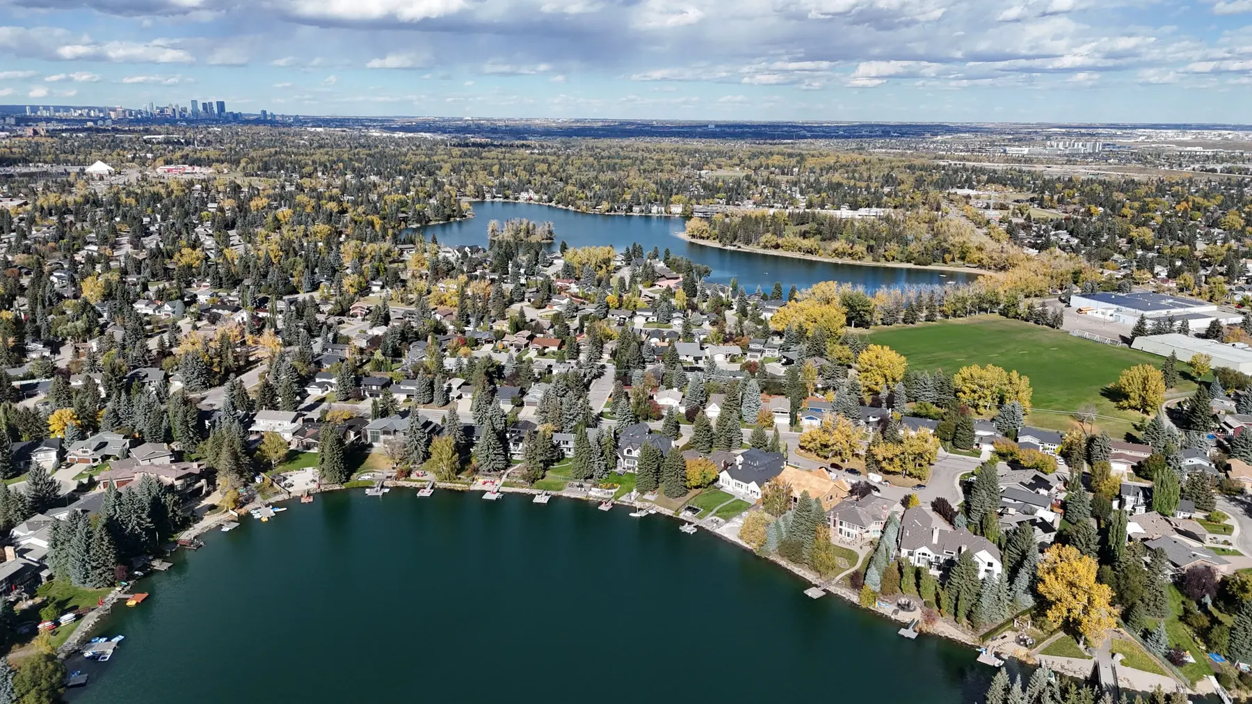 Aerial view of Lake Bonavista homes along the lake, with downtown Calgary on the horizon